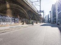 graffiti covered brick wall and gate under an overpass in an urban area with sun light