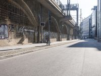 graffiti covered brick wall and gate under an overpass in an urban area with sun light