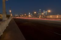 a city bridge at dusk has cars driving along it with buildings lit up in the distance