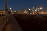 a city bridge at dusk has cars driving along it with buildings lit up in the distance