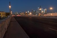 a city bridge at dusk has cars driving along it with buildings lit up in the distance