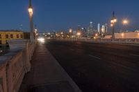 a city bridge at dusk has cars driving along it with buildings lit up in the distance