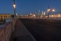 a city bridge at dusk has cars driving along it with buildings lit up in the distance