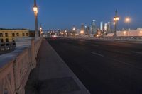 a city bridge at dusk has cars driving along it with buildings lit up in the distance