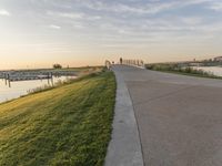 the view of a bridge across the grass fields from a path at sunset in a city park