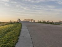 the view of a bridge across the grass fields from a path at sunset in a city park