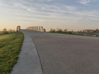 the view of a bridge across the grass fields from a path at sunset in a city park