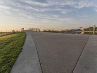 the view of a bridge across the grass fields from a path at sunset in a city park