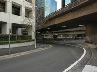 a street with a bridge above it next to a tall building at the corner of a busy city street