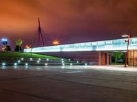 a bridge over a large building with lights on at night time with grass around the walkway and street light fixtures