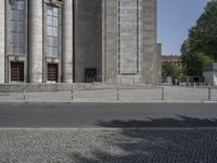 a man in green shirt skateboarding down a sidewalk next to some building facades and columns