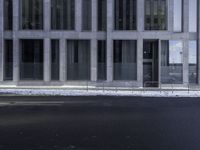 an empty street in front of a large office building, while a man takes his picture on his cell phone