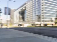 the side view of a street with traffic passing by a city building in motion bluring