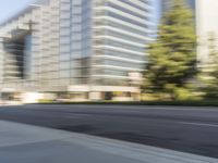 the side view of a street with traffic passing by a city building in motion bluring