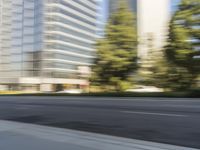 the side view of a street with traffic passing by a city building in motion bluring