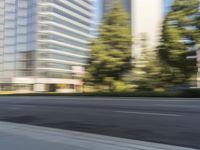 the side view of a street with traffic passing by a city building in motion bluring