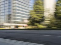 the side view of a street with traffic passing by a city building in motion bluring