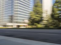 the side view of a street with traffic passing by a city building in motion bluring