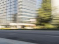 the side view of a street with traffic passing by a city building in motion bluring