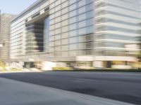 the side view of a street with traffic passing by a city building in motion bluring