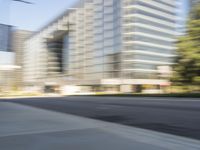 the side view of a street with traffic passing by a city building in motion bluring