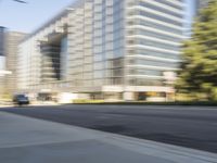 the side view of a street with traffic passing by a city building in motion bluring