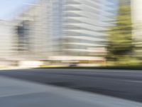 the side view of a street with traffic passing by a city building in motion bluring