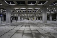 an empty concrete floor and ceiling area in a city building at night with lights on it