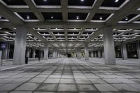 an empty concrete floor and ceiling area in a city building at night with lights on it