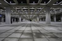 an empty concrete floor and ceiling area in a city building at night with lights on it