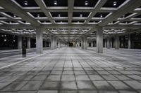 an empty concrete floor and ceiling area in a city building at night with lights on it