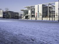 a paved area next to buildings on a clear day with snow on the ground and one side has tall glass windows