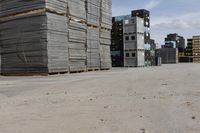 a pile of pallets and some buildings are in the distance in an empty lot