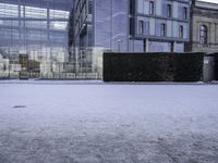 an outdoor courtyard covered with snow and ice, next to two buildings and a hedge