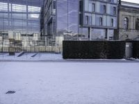 an outdoor courtyard covered with snow and ice, next to two buildings and a hedge