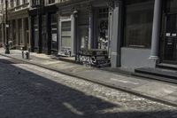 two people walking down the sidewalk beside buildings and benches on the street in front of them