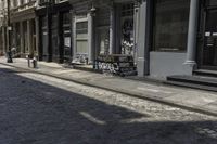 two people walking down the sidewalk beside buildings and benches on the street in front of them