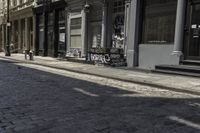 two people walking down the sidewalk beside buildings and benches on the street in front of them