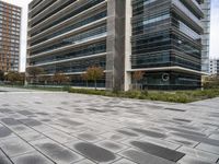 the sidewalk in front of the office building with modern architecture near it with the sky reflecting on the building