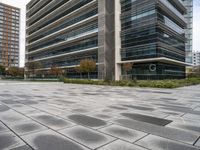 the sidewalk in front of the office building with modern architecture near it with the sky reflecting on the building