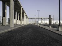 a large wide paved sidewalk lined with tall concrete columns and concrete poles and lamps on either side