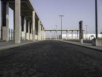 a large wide paved sidewalk lined with tall concrete columns and concrete poles and lamps on either side