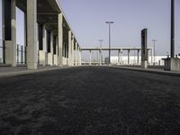 a large wide paved sidewalk lined with tall concrete columns and concrete poles and lamps on either side