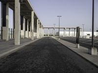 a large wide paved sidewalk lined with tall concrete columns and concrete poles and lamps on either side