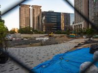 construction cranes are next to a sidewalk in the city and behind the fence that is a tarp