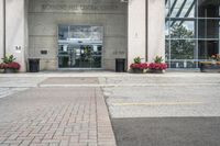 people cross the street in front of an entrance to the city court building, with potted flower plants lining either side of the entry way