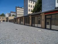 the sidewalk is paved with stones and has a bench in front of it, with no people inside