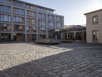 a cobblestone courtyard with two buildings and a park bench in the foreground