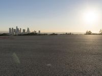 the person riding his bike through the parking lot near a city skyline as he goes off into the distance