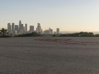 the person riding his bike through the parking lot near a city skyline as he goes off into the distance